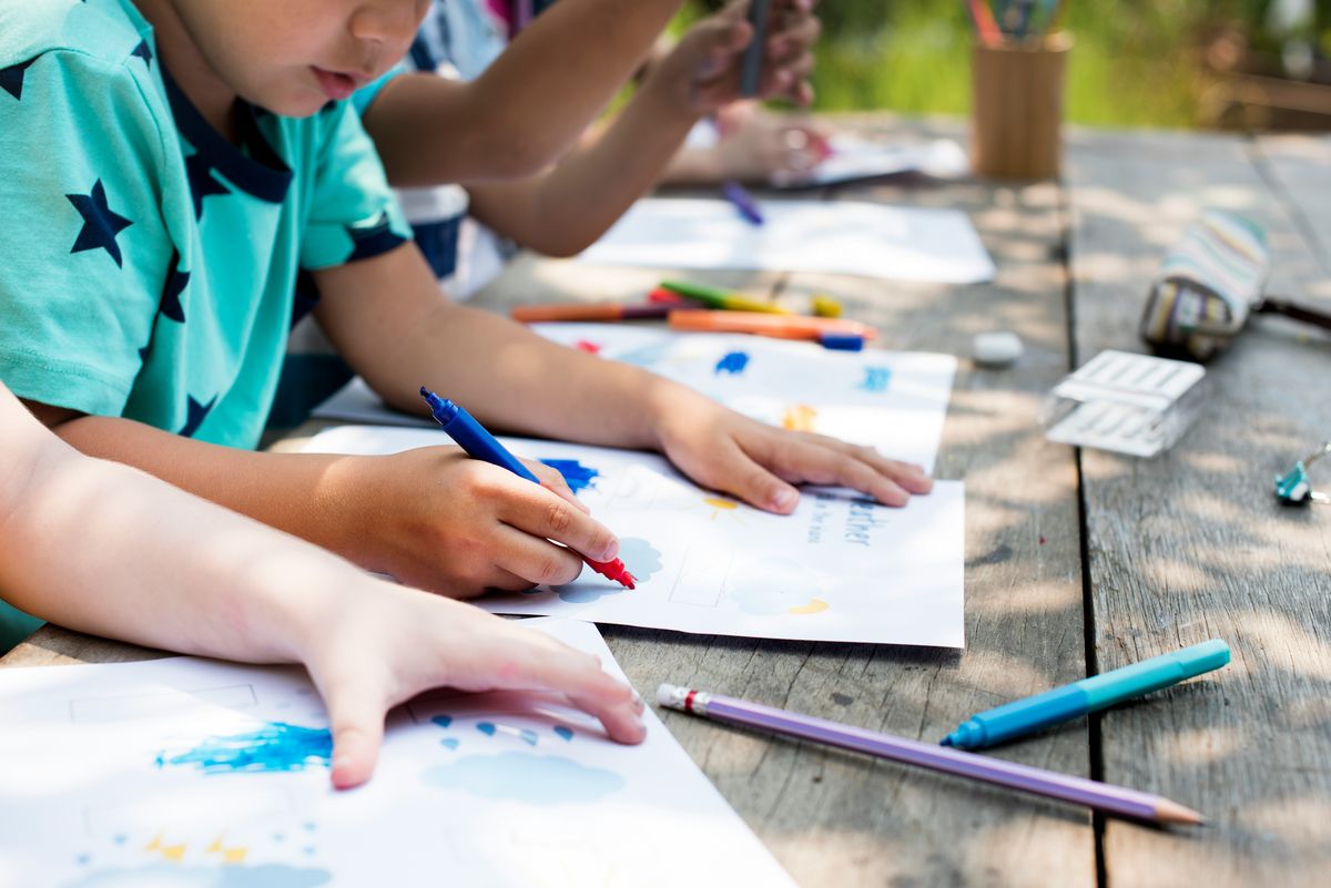 Children's hands drawing with coloured pencils on a dark wood table
