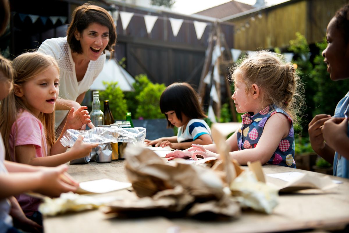 A teacher and three children working together at an outdoor table