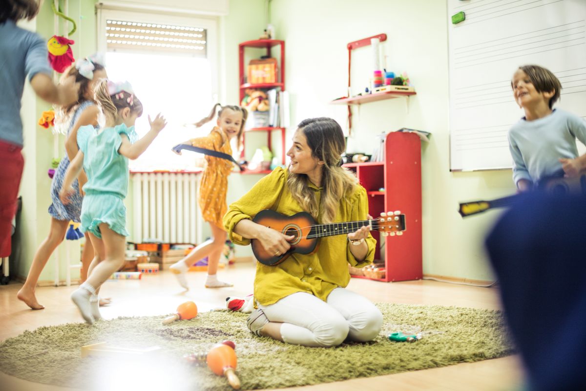 An adult playing ukulele while children move to the music