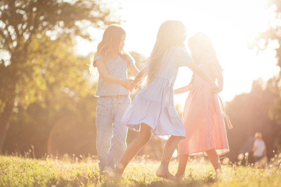 Three children holding hands in a ring in a sunlit meadow