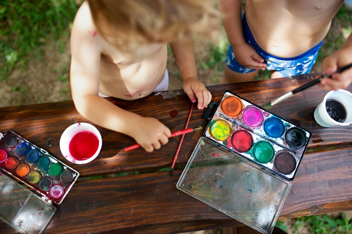 Two children painting with watercolours at a dark wood table