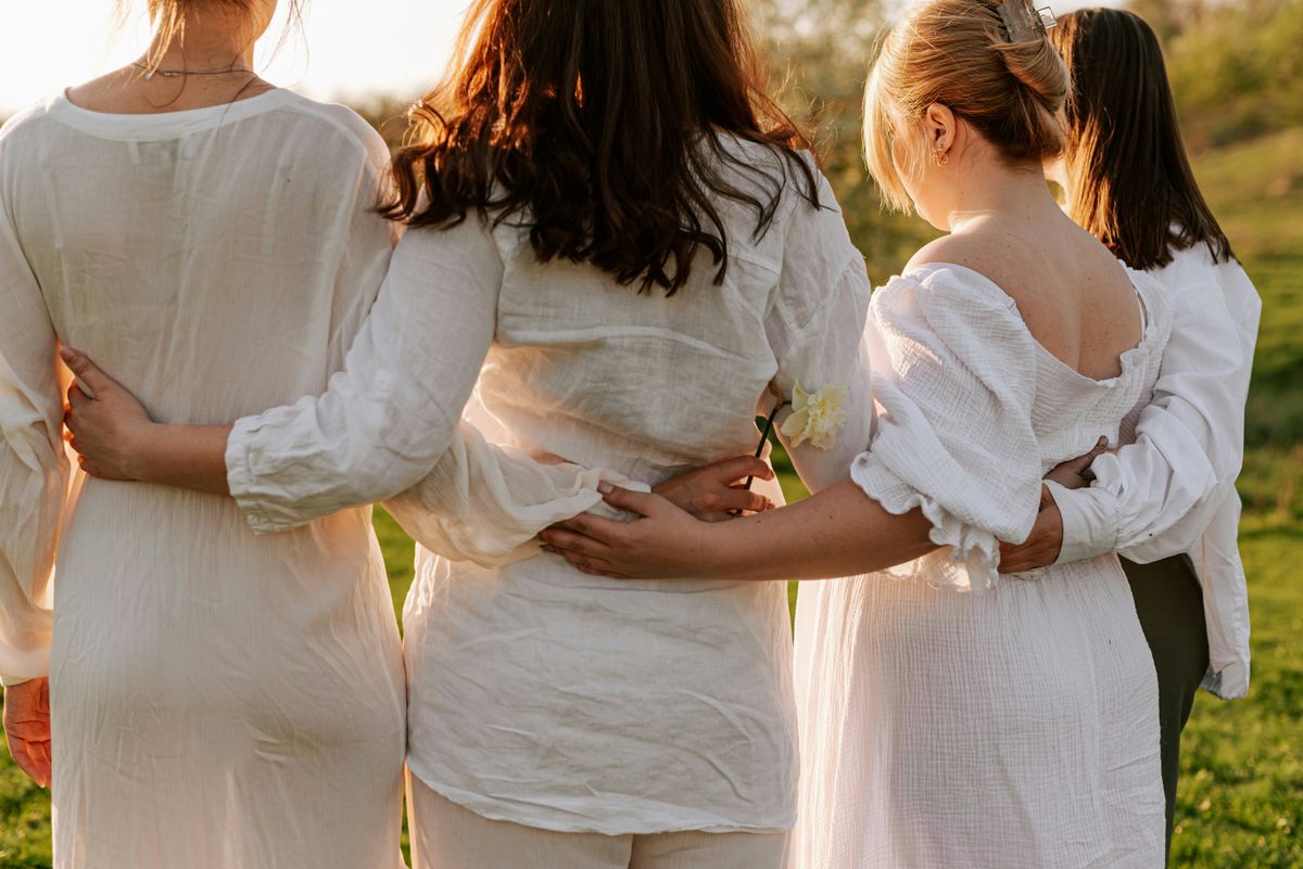 Four women standing arm in arm, backs to the camera